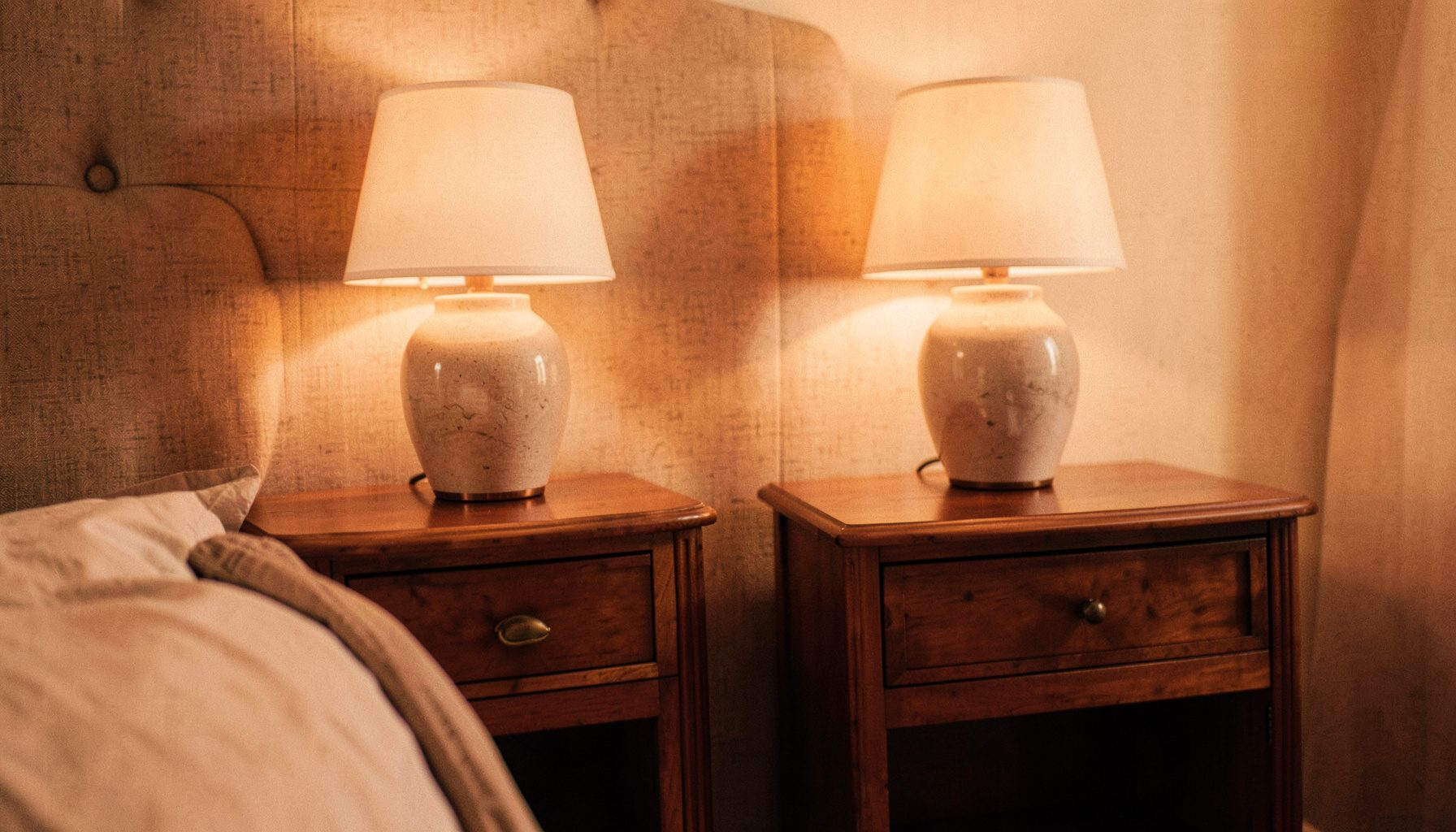 A pair of elegant wooden bedside tables flanking a fabric headboard, each topped with a ceramic table lamp
