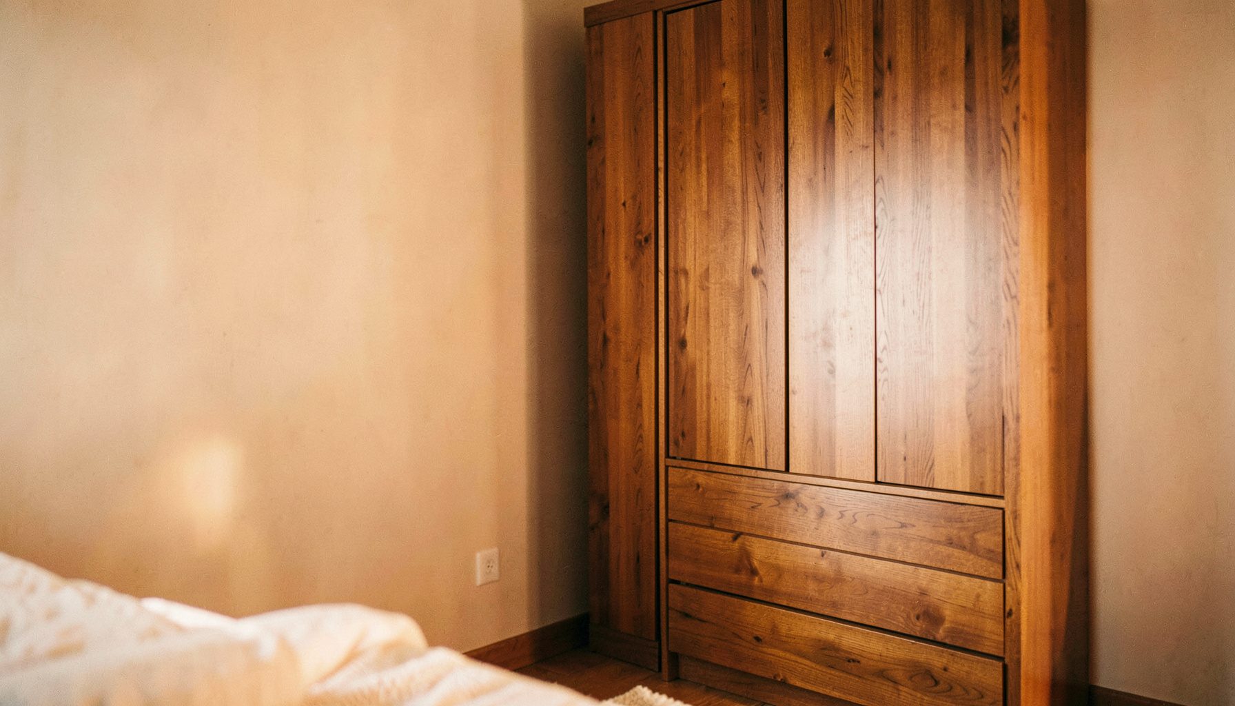 A light-filled bedroom corner featuring a tall wooden wardrobe and matching chest of drawers in a warm oak finish